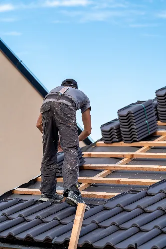 A roofer securing a heavy duty tarp over a damaged section of a tiled roof during an emergency roof repair to stop water from entering the property.